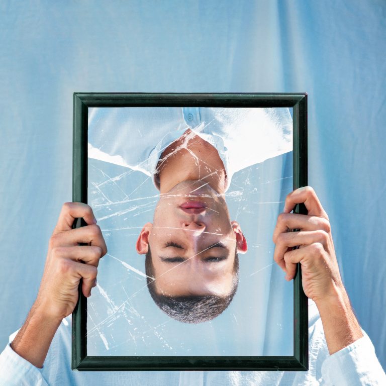Man holding an upside down broken mirror with his own reflection on it