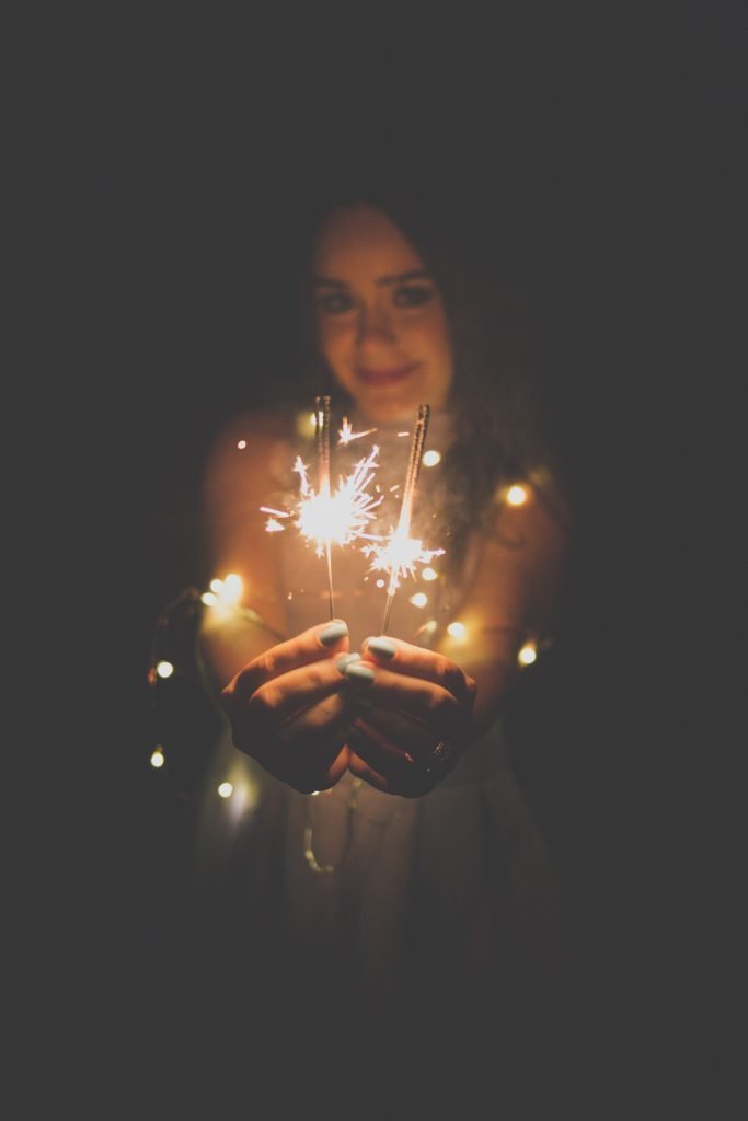 woman carrying two lighted sparklers against black background