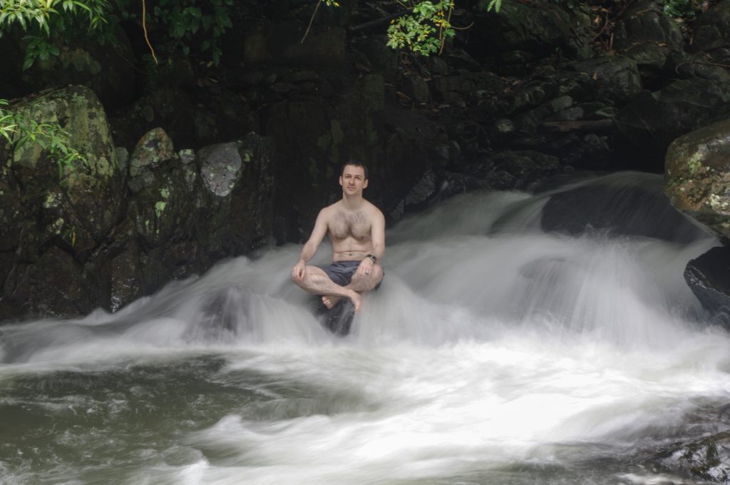 man sitting on rock in waterfall: a form of hydrotherapy
